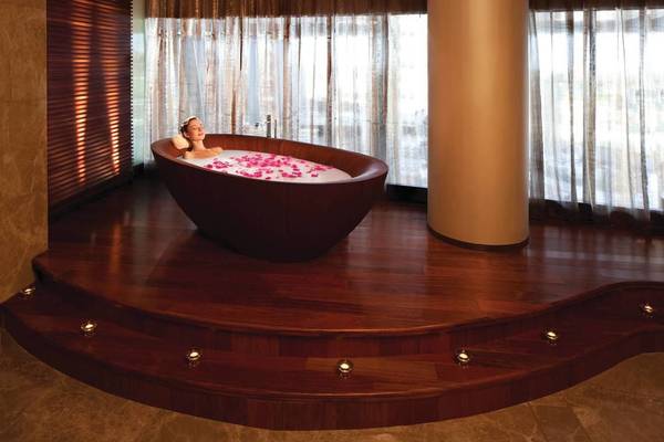 Eine Frau genießt ein Bad in einer runden Badewanne im Conrad Abu Dhabi Etihad Towers, umgeben von Rosenblättern.