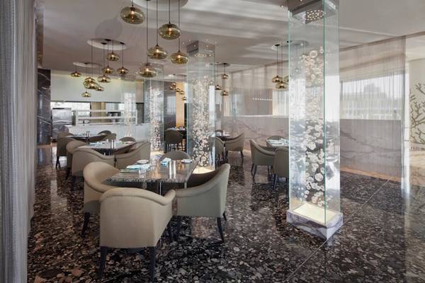 Innenansicht des Restaurants im Conrad Abu Dhabi Etihad Towers mit Marmorboden, modernen Stühlen und Tischen, Glaswänden und Beleuchtung.