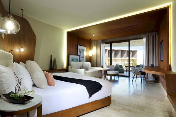 Innenansicht des Schlafzimmers im TRS Coral Hotel mit großem Bett, Sitzbereich und Glastür zum Balkon.