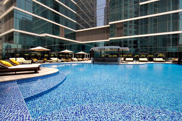 Außenpool des Taj Dubai Hotels mit Lounge-Liegen und Sonnenschirmen.