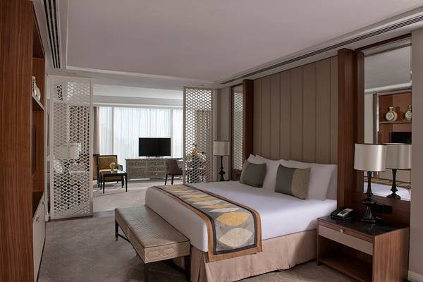 Innenansicht eines Hotelzimmers im Taj Dubai mit großem Bett, Fernseher, und Möbeln.