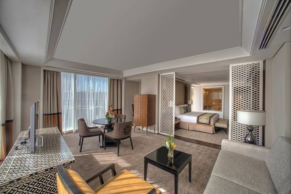 Innenansicht eines Zimmers im Taj Dubai Hotel mit Bett, Tisch, Stühlen und Fernseher.
