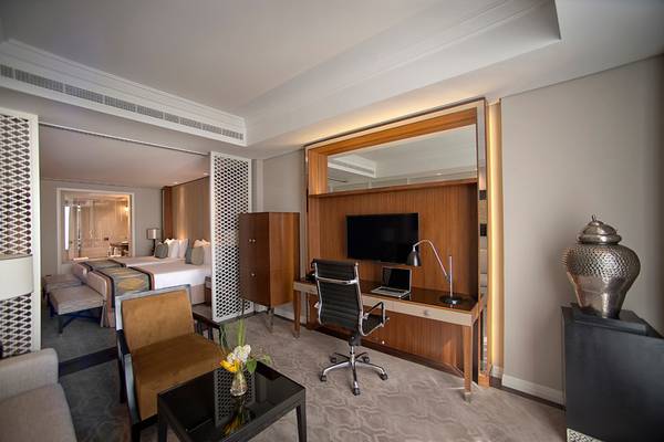 Innenansicht eines Hotelzimmers im Taj Dubai mit Schreibtisch, Stuhl, Fernseher und Bett.