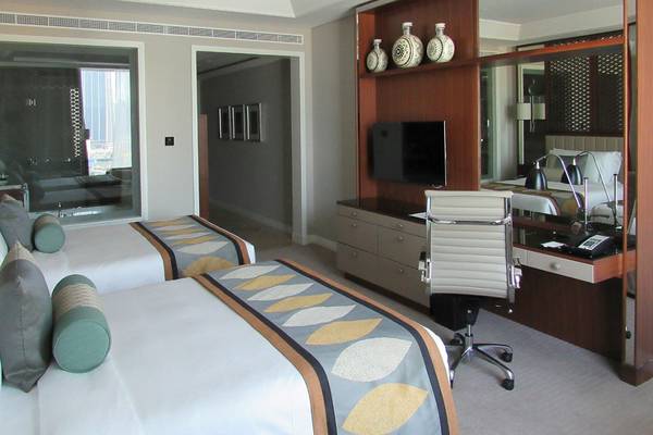 Innenansicht eines Hotelzimmers im Taj Dubai mit zwei Betten, Schreibtisch und Fernseher.