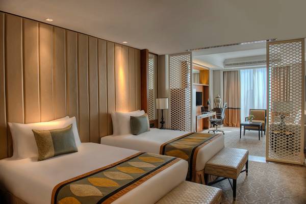 Innenansicht eines Hotelzimmers im Taj Dubai, mit zwei Betten, Schreibtisch und Aussicht auf einen Balkon.