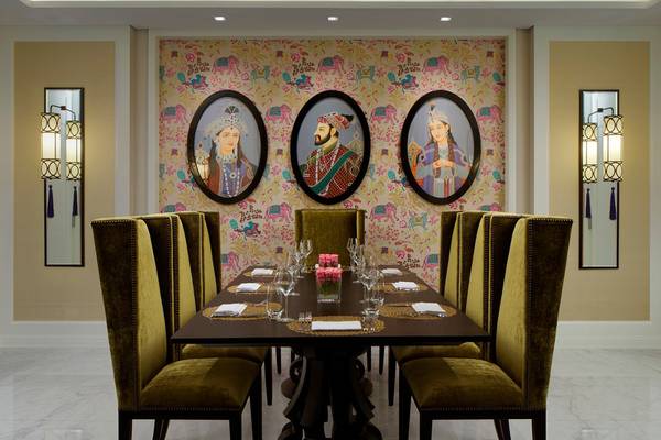Speisesaal des Taj Dubai mit drei Porträts an der Wand, gedeckter Tisch mit Wein und Kerzen.