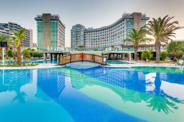 Ein Swimmingpool vor dem Sherwood Exclusive Lara Hotel mit einem Holzsteg und Palmen.