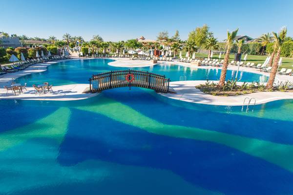Pool des Sherwood Exclusive Lara Hotels mit Sonnenliegen, Schirmen und einer Brücke.