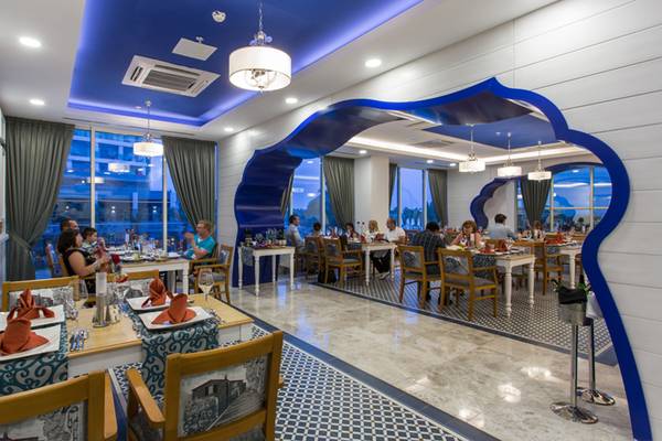 Restaurant im Sherwood Exclusive Lara Hotel mit blauen Akzenten und Gästen, die an Tischen sitzen.