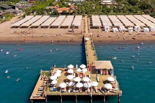 Luftaufnahme des Sherwood Exclusive Lara Hotels mit Strand und vielen Gästen, die schwimmen und sonnenbaden.