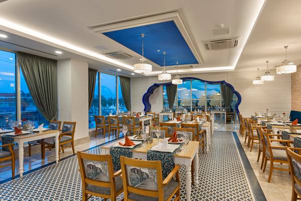 Innenansicht des Restaurants des Sherwood Exclusive Lara Hotels mit blauer Decke und großen Fenstern.