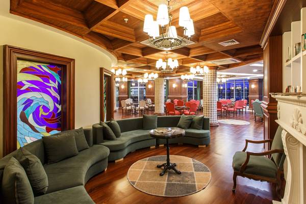 Innenbereich des Sherwood Exclusive Lara Hotels mit grüner Couch, Tisch und farbiger Glasmalerei.