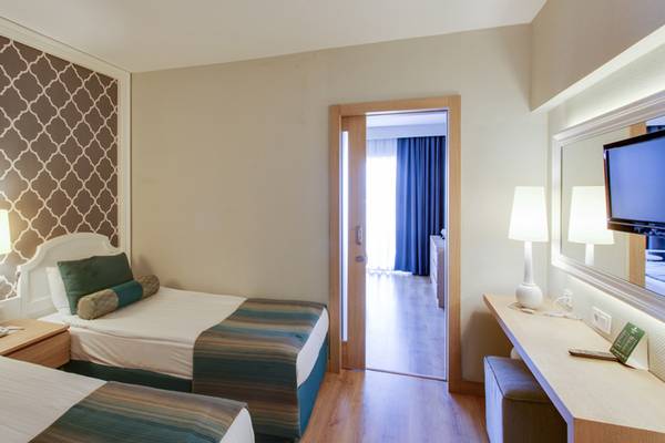 Innenansicht eines Doppelzimmers im Sherwood Exclusive Lara Hotel mit zwei Betten, Dekor, Lampen und Fernseher.