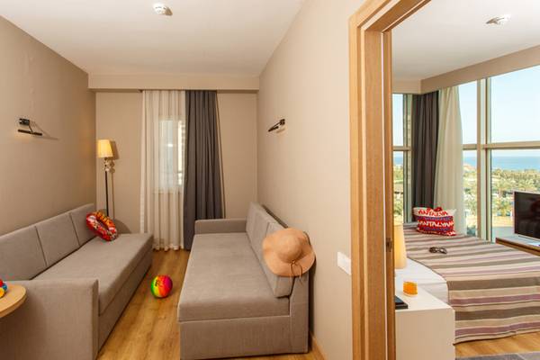 Innenansicht eines Zimmers im Sherwood Exclusive Lara Hotel mit zwei Sofas, einem Tisch, Spielzeug und einem Blick auf das Meer.
