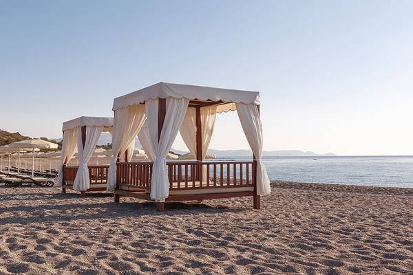 Zwei Strandbetten mit weißen Vorhängen und Sonnenschirmen auf dem Strand des Boutique 5 Hotels & Spa.