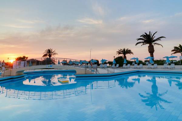 Ein Swimmingpool im Creta Star Hotel bei Sonnenuntergang mit blauen Sonnenschirmen und Palmen im Hintergrund.