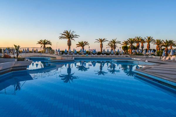 Swimmingpool im Creta Star Hotel bei Sonnenuntergang mit Palmen und Sonnenschirmen.