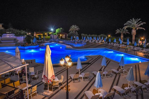 Nachtansicht des beleuchteten Swimmingpools des Creta Star Hotels mit Sonnenliegen und Schirmen.