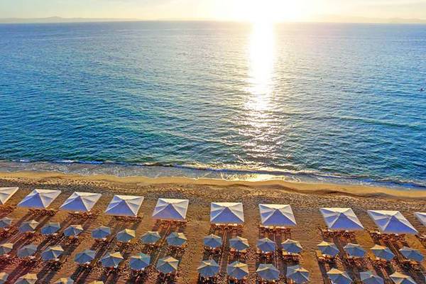 Luftaufnahme des Creta Star Hotels mit Sonnenuntergang über dem Meer und vielen Sonnenschirmen am Strand.