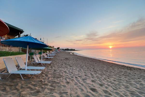 Strand des Creta Star Hotels bei Sonnenuntergang mit weißen Liegestühlen und blauen Sonnenschirmen