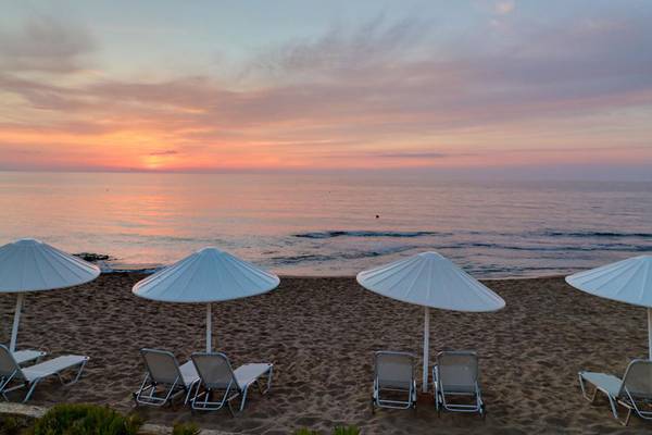 Sonnenuntergang am Strand des Creta Star Hotels mit weißen Sonnenschirmen und Liegestühlen.