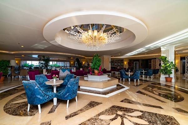 Lobby des Seamelia Beach Resort & Spa mit zentralem Kronleuchter, blauen Stühlen und Tischen sowie Pflanzen.