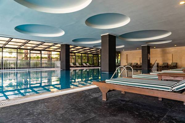 Poolbereich im Seamelia Beach Resort & Spa mit Lounge-Liegen und einer Glasfassade.