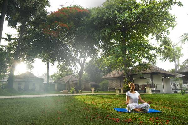 Frau praktiziert Yoga im Garten des Jimbaran Puri Hotels in Bali.