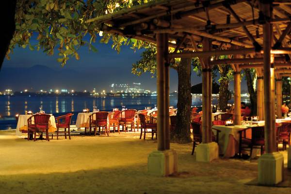 Abendessen unter offenem Himmel im Jimbaran Puri, Bali, mit Blick auf das Wasser und die Stadt