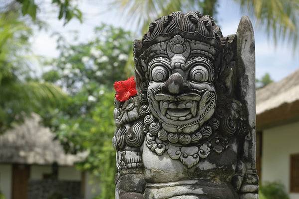 Balinesische Skulptur mit einer roten Hibiskusblüte im Jimbaran Puri Hotel, Bali.