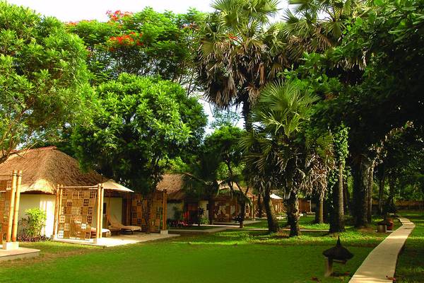 Außenbereich des Jimbaran Puri Hotels in Bali mit Hütten und grünem Rasen.