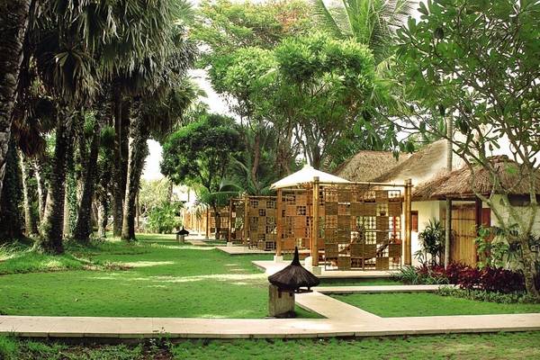 Außenbereich des Jimbaran Puri Hotels in Bali mit tropischen Bäumen und gepflasterten Wegen.