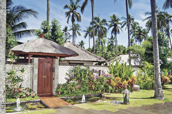 Eingang des Jimbaran Puri, A Belmond Hotel, Bali mit tropischen Pflanzen und Palmen im Hintergrund