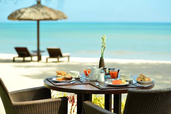 Frühstück am Strand im Jimbaran Puri Hotel mit Blick auf das Meer und Sonnenschirmen.