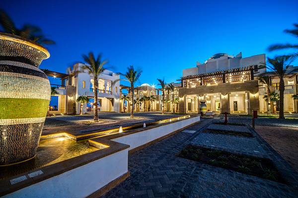 Eingang des Ancient Sands Golf Resorts bei Nacht mit beleuchtetem Brunnen und Palmen.