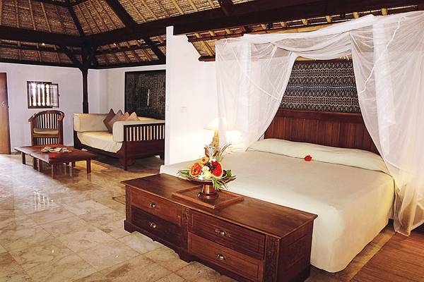 Ein elegantes Zimmer im Jimbaran Puri Hotel in Bali mit einem großen Bett, einem Nachttisch und einer Couch.