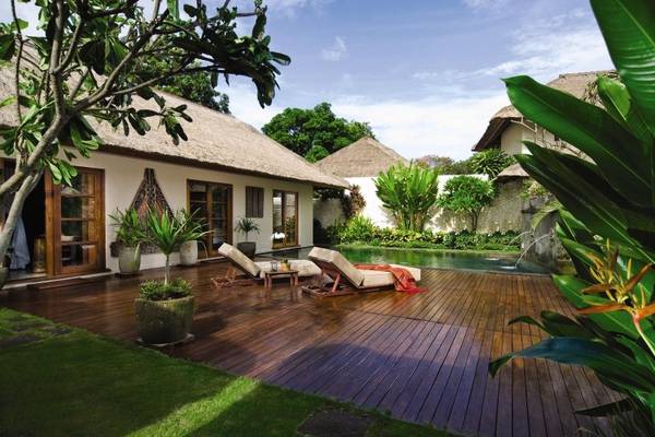 Terrasse mit zwei Liegen im Jimbaran Puri, Bali, umgeben von Pflanzen und einem kleinen Pool.