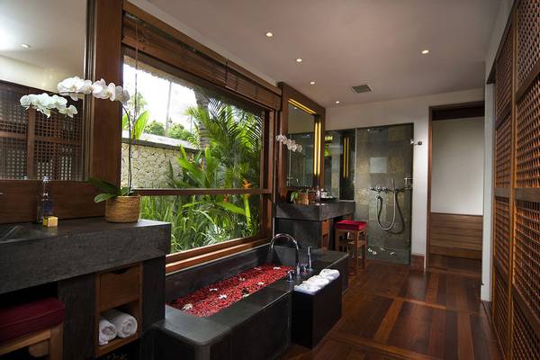 Badezimmer im Jimbaran Puri Hotel, Bali mit großer Fensterfront und Blick auf die Natur.