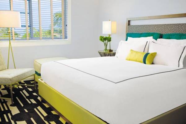 Helles Zimmer im Kimpton Surfcomber Hotel mit Bett, Lampen und Fenster mit Jalousien.