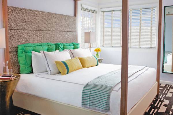 Schlafzimmer im Kimpton Surfcomber Hotel mit Himmelbett, grünen Kissen und weißen Decken.