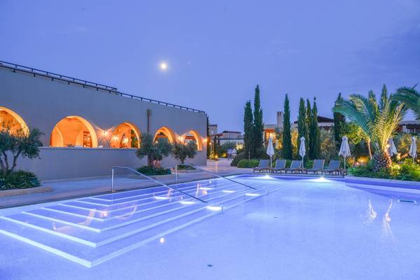 Außenpool des Westin Resorts Costa Navarino bei Nacht mit illuminierten Arkaden und Lounge-Stühlen.