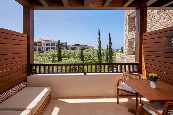 Aussicht vom Balkon des Westin Resort, Costa Navarino auf eine gepflasterte Terrasse mit Tisch, Stühlen und einem Blumentopf.