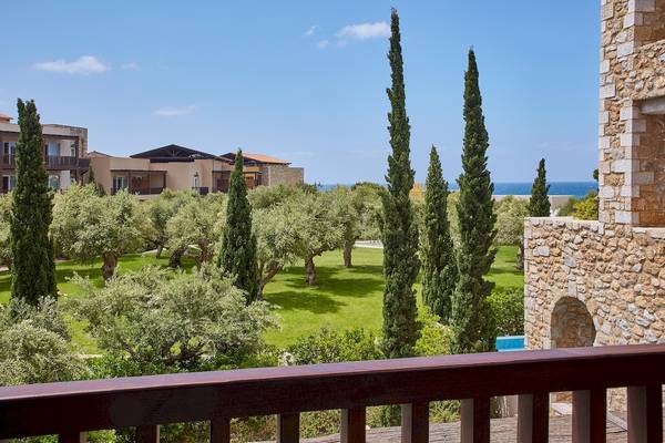 Blick vom Balkon des Westin Resorts Costa Navarino auf eine grüne Parklandschaft mit Zypressen und Gebäuden am Horizont.