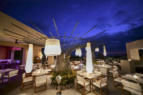 Abendaufnahme des Restaurants im Westin Resort, Costa Navarino mit beleuchteten Tischen und Stühlen.