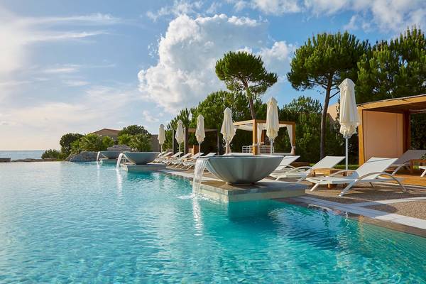Außenpool des Westin Resorts in Costa Navarino mit weißen Sonnenliegen und Schirmen.