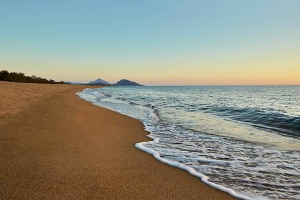 Strand des Westin Resorts Costa Navarino bei Sonnenuntergang mit sanften Wellen und Bergen im Hintergrund