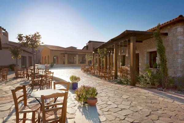 Außenbereich des Westin Resorts in Costa Navarino mit Holztischen und Stühlen.