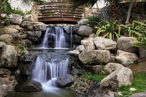 Wasserfall im Hotel JA Palm Tree Court mit einer Brücke aus Holz über den Wasserfall.
