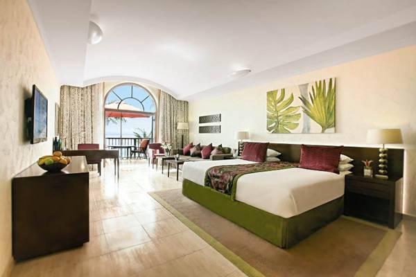 Innenansicht eines Zimmers im JA Palm Tree Court Hotel mit Bett, Tisch und Fenster mit Balkon.