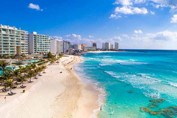 Luftaufnahme des Riu Cancun Hotels am Strand mit weißen Sand, blauem Ozean und Gebäuden im Hintergrund.